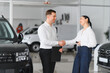 © Serhii - Salesman and customer shaking hands in a car dealership showroom