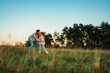 © DusanJelicic - Mother is kissing her daughter on the forehead while standing in a meadow at sunset, with trees in the background, enjoying a peaceful moment together