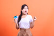 © Ajab - A woman holds her credit card looking very excited, with an open mouth and a closed fist, and a surprised face, isolated on orange background