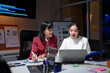 © Crystal - Two Asian businesswomen analyzing financial charts on a laptop, working late and smiling in a modern office