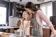 © lordn - A mother and her daughter are baking together in a modern kitchen, sharing a joyful moment while mixing ingredients in a bowl.