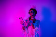 © deagreez - Elegant young woman in lace gown holding phone against neon pink and purple backdrop
