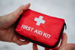 © Aleksey - A person is firmly holding a bright red first aid kit tightly in their hands, ready to provide any necessary medical assistance or support in case of an emergency situation