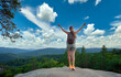 © bilanol - Young woman hiker standing alone with outstretched hands on mountain footpath enjoying view of evening nature on wilderness trail. Active way of life concept