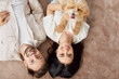 © Studio Romantic - Happy childless childfree family couple with pet dog enjoying cozy relationship harmony. Indoor overhead shot from above smiling young man and woman lying on brown rug with little beige furry friend