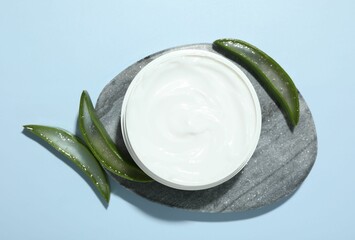 Wall Mural - moisturizing cream with extract of aloe vera and cut leaves on light blue background, flat lay
