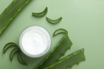 Wall Mural - moisturizing cream with extract of aloe vera in jar and cut leaves on green background, flat lay
