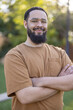 © Bogdan Pictures - A smiling man stands confidently outdoors, his arms crossed and a relaxed demeanor, wearing stylish glasses and a brown shirt, while surrounded by vibrant greenery illuminated by soft sunlight