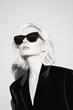 © Leli - Stylish blonde woman looking up while wearing black sunglasses and a velvet suit.