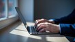 © Anusa - Person Typing on Laptop by Window on Sunlit Desk Surface