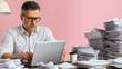 © Olha Havelia - Photo of an overweight middle-aged man sitting at his desk in a pink office, searching for documents on the laptop screen, surrounded by piles and stacks of papers. Professional ph