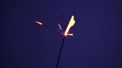 Poster - Burning sparkler against a dark blue background, bright and festive mood