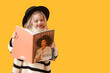 © Pixel-Shot - Cute little girl in adult clothes reading magazine on yellow background