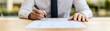 © Passakorn - A person in a white shirt is signing a document on a wooden table, emphasizing professionalism and focus in a work environment.