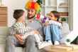 © Pixel-Shot - Little children with megaphone shouting on their happy father in clown wig at home. April fool's Day prank