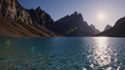 Wall Mural - Sunlit mountain peaks reflecting on a tranquil lake with clear blue water. Peaceful nature