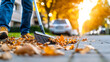 © Poonnoi - Autumn cleanup action worker sweeping leaves on a city sidewalk in early morning light urban environment close-up view seasonal change