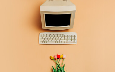 vintage pc and tulips on brown background, top view. monitor and keyboard as in 90s
