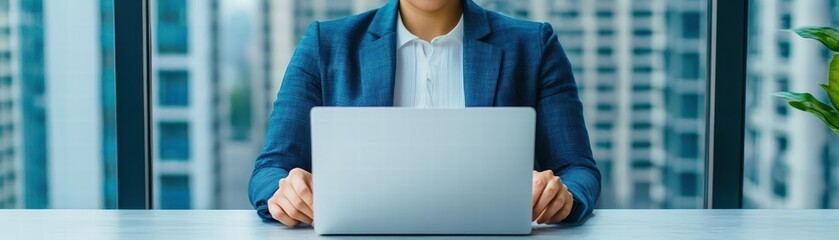 Fototapete - Professional woman sitting at a table working on a laptop with a concentrated expression in a modern workspace
