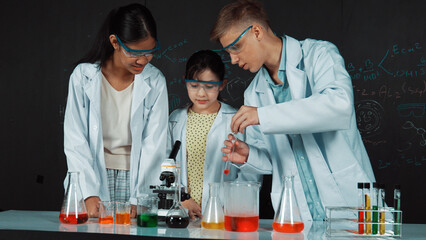 Poster - smart girl pour colored solution in to beaker while diverse student excited about doing experiment. 