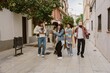 © Drobot Dean - Five casually dressed multiethnic friends in their late 20s, three men and two women, walk together on a city street, one man holding a small dachshund dog, next to buildings, during daytime.