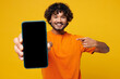 © ViDi Studio - Young Indian man wear orange t-shirt casual clothes hold in hand use point on mobile cell phone with blank screen workspace area show thumb up isolated on plain yellow background. Lifestyle concept.