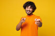 © ViDi Studio - Young smiling fun happy Indian man he wear orange t-shirt casual clothes point index finger camera on you motivating encourage isolated on plain yellow background studio portrait. Lifestyle concept.