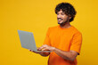 © ViDi Studio - Young smiling fun happy IT Indian man he wear orange t-shirt casual clothes hold use work on laptop pc computer chatting online isolated on plain yellow background studio portrait. Lifestyle concept.