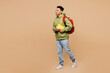 © ViDi Studio - Full body side view young smart boy student wearing green casual clothes backpack bag hold books walking going isolated on plain pastel light beige background. High school university college concept.
