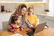 © New Africa - Single mother working on laptop and her daughters at table in kitchen