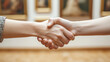 © Hanzala - Two hands shaking with a soft-focus art gallery backdrop, denoting cultural agreements.
