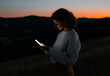 © Amy - Young woman using smartphone outdoors at sunset, blending technology and nature