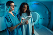 © pressmaster - Medical professional in scrubs guiding patient with digital tablet near MRI scanner for procedure. Medical setting with technological equipment
