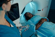 © pressmaster - Woman lying in MRI machine undergoing scan procedure in modern medical facility, with technician holding control panel and carefully monitoring scan process