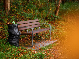 Wall Mural - bench in a forest park made of plastic brown color panels on metal frame, black plastic bag for rubb