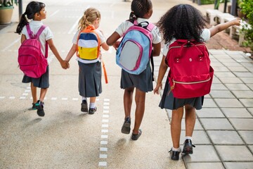 Poster - Four cute girls with backpacks walk together on a path. School bags, diverse children, and friendship are highlighted in this cheerful scene. Cute diverse little school girls with backpacks.