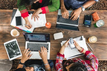 Poster - An Indian group of friends, collaborate at a wooden table, using laptops and smartphones for a productive brainstorming session. Indian group using devices and brainstorming together