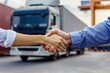 © AlAfiq - Business professionals shaking hands to symbolize partnership in logistics and transportation industry with truck in background against port setting