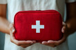 © Harmony Studio - A person holds a bright red first aid kit featuring a white cross, symbolizing safety and preparedness