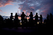 © Irina - Silhouettes of people dancing a circle folk dance in the street at sunset.