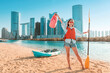 © EdNurg - Young woman enjoys kayaking in front of Abu Dhabi skyline, holding a paddle and a waterproof bag