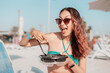 © EdNurg - Happy young woman pointing at her takeaway food with a plastic fork while enjoying lunch on a sunny beach