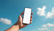 © Maryna - Man hand holds phone mockup against blue sky with clouds. Mobile device with blank white screen for app presentation. Summer outdoors vacation, modern tech copy space.