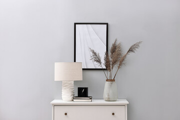 Poster - console table with lamp, clock, books and vase near light grey wall. interior design