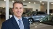© GS-Studio - Smiling Salesman in Dealership: A professional salesman, radiating confidence and expertise, stands in a car dealership, the sleek vehicles subtly highlighting the setting.
