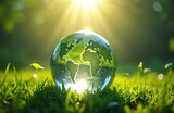 Glass globe lies on green grass under bright sun. Symbol of nature, ecology, environment, sustainability, conservation, natural resources, climate change awareness and eco-friendly lifestyle.