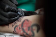 © ces - Close up tattoo master professional tattoo artist in black gloves making a rose tattoo on a man's forearm. He is holding a tattoo machine.