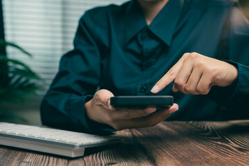 Poster - Person Using Smartphone with Focused Expression in Modern Office Setting with Computer Nearby, Business concept