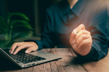 Poster - Close-Up of Hand Holding Pen Near Laptop on Wooden Table in Modern Office Setting, Business concept