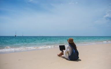 Wall Mural - a female traveler using and working on laptop computer while sitting on the beach